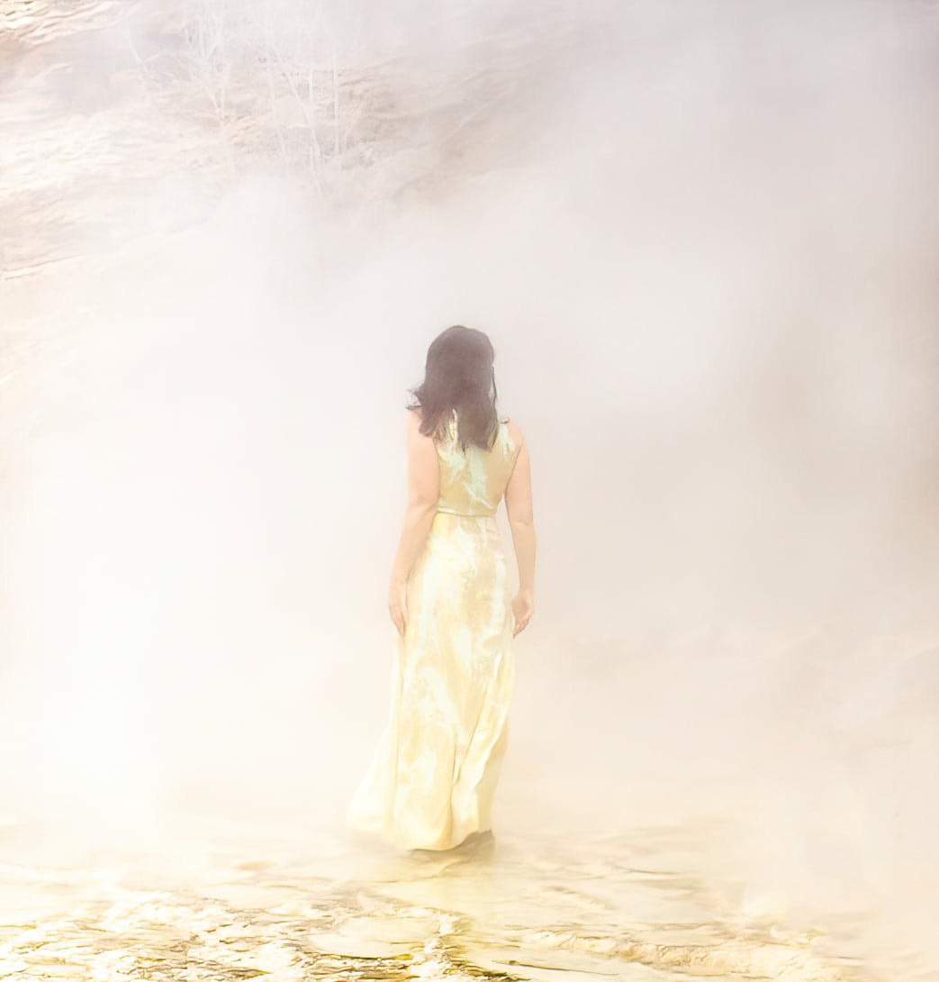 a girl in a gold dress stands in a steaming hot spring