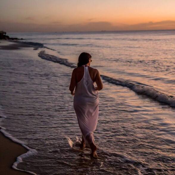 a girl walks along the beach during sunset