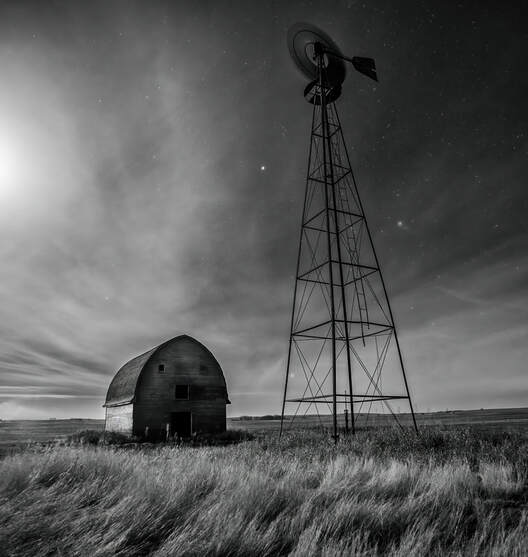A windmill and barn stand in a field under the night sky
