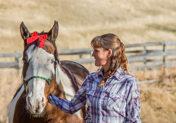 a girls smiles at her horse who's wearing a red bow