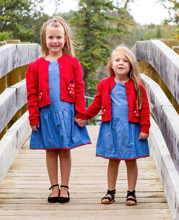 sisters, in matching dresses, hold hands on a bridge