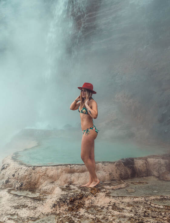girl poses in a bikini and red hat in front of hotsprings