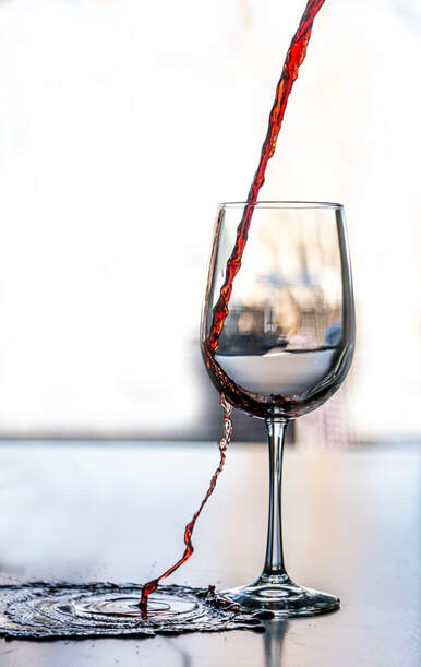 Red wine spills over a wine glass creating a puddle at the base of the glass