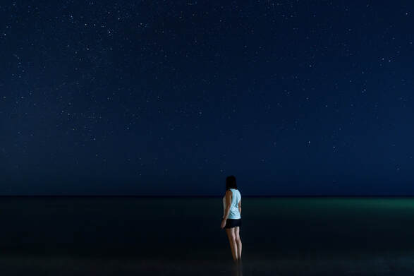 a girls legs disappear into the sea while she stands under the stars