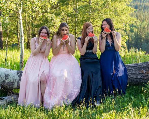 four girls in grad dresses, eat watermelon on a log
