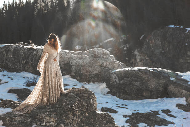 sunlight washes over a girl in a long gown standing on a cliff