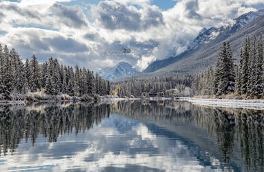 A first snowfall with cloudy skies reflects in the Bow River