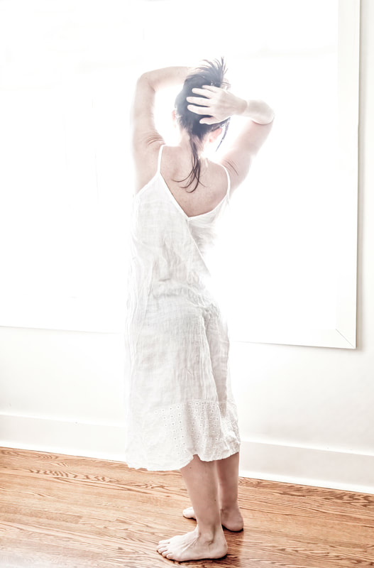 a girl in a white dress holds her dark hair up in  an over exposed image