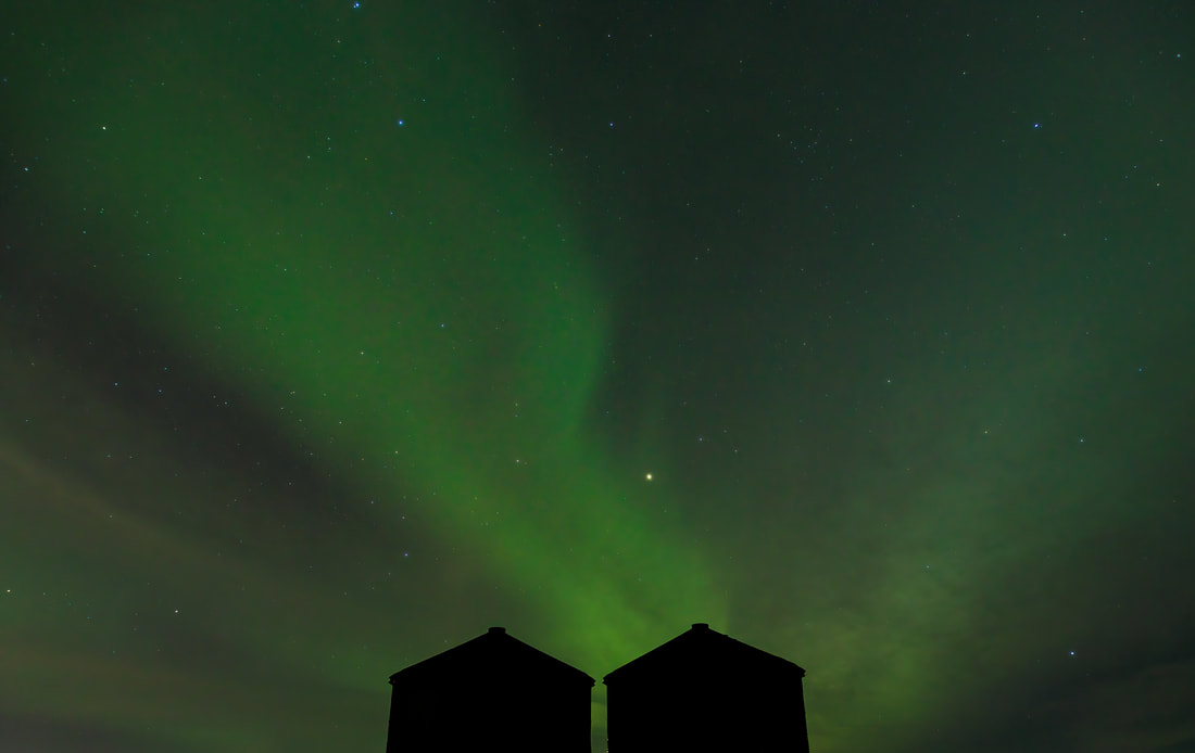 Two silhouetted silos sit below an Aurora storm