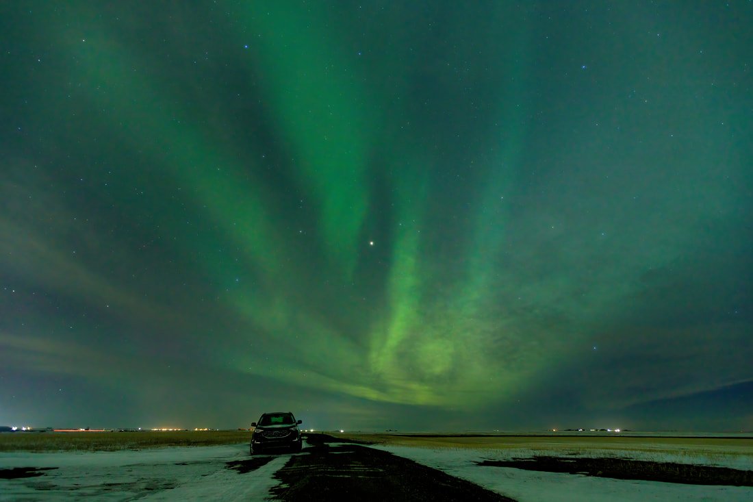 Northern lights above a gravel road with a vehicle parked on the side