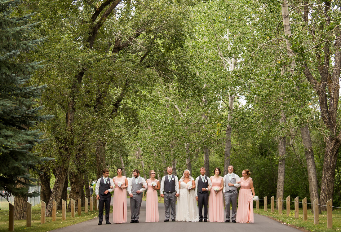 the bridal party stands under a grove of trees