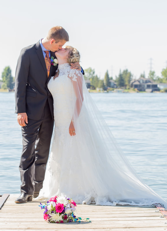 the wedding couple kiss on a dock in front of a lake
