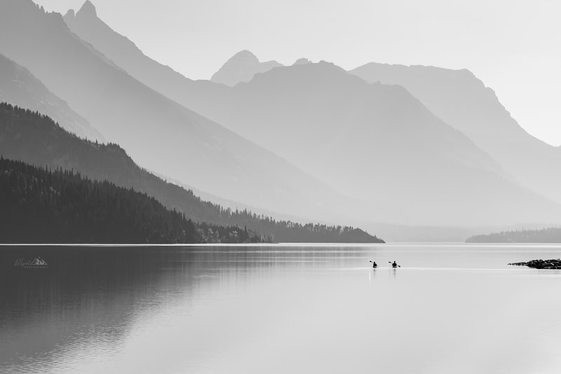 two kayakers paddle out into a lake, wild fire smoke hangs in the mountains