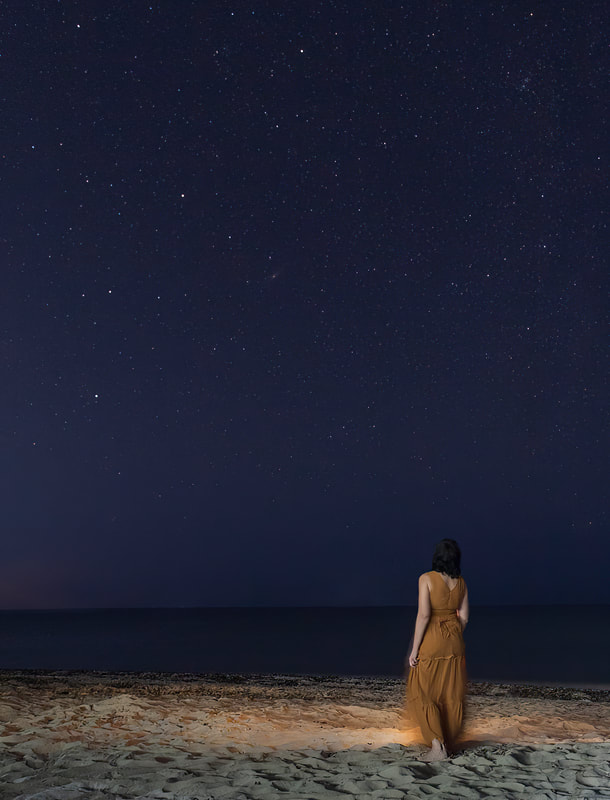 a girl stargazes while standing in the sand