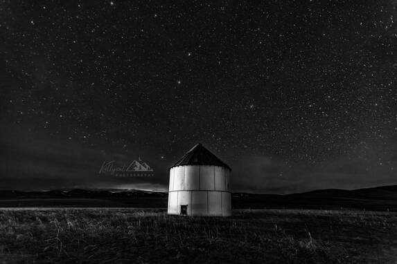 A grain silo sits in a field under a brilliant sky full of stars