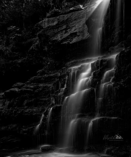 a black and white image of a waterfall plunging over a cliff
