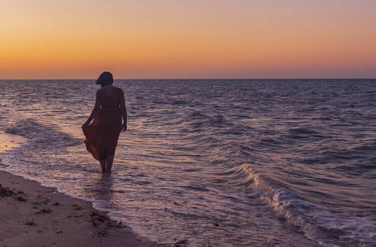 A woman stands in the sea while her dress sways in the breeze